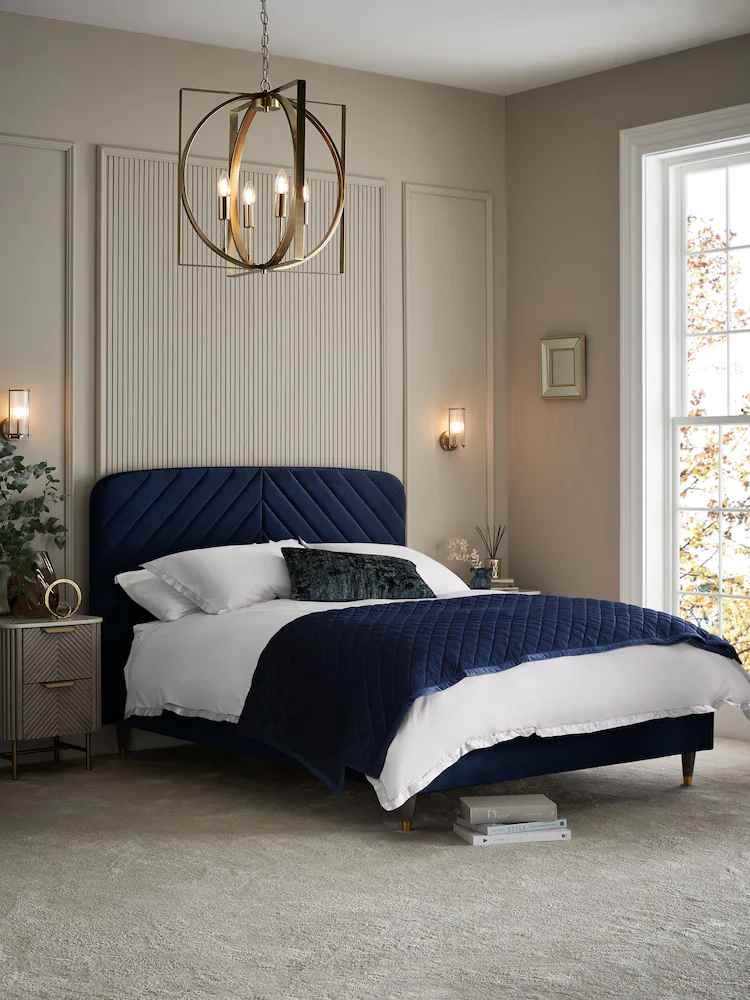 A blue velvet headboard in grey bedroom with and lights o the wall