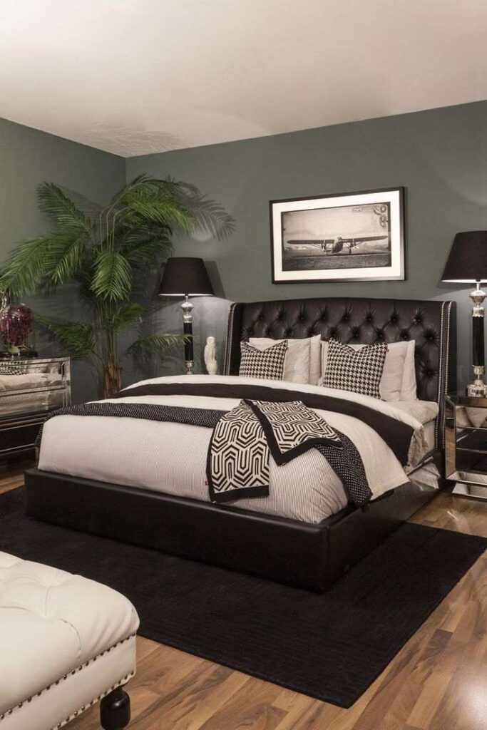 A sage green bedroom with black headboard with lamp on the side table and wooden floor 