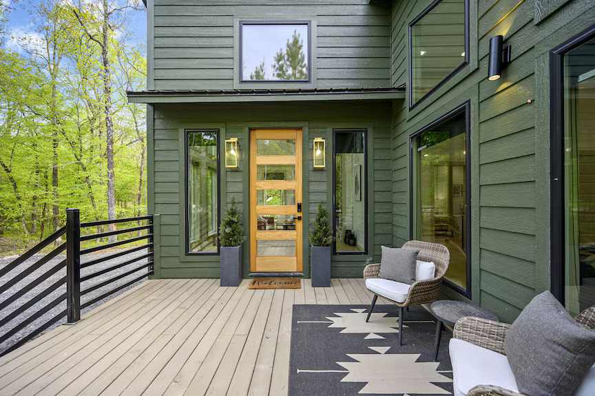 A green house wit wooden porch and yellow door and windows 