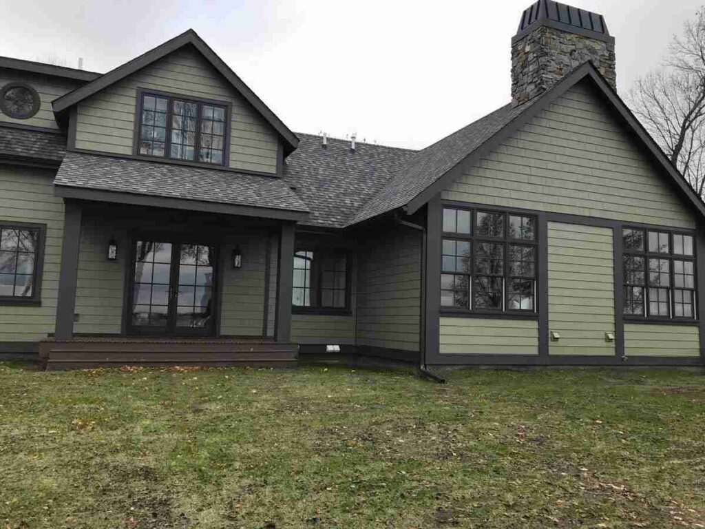 A green house with black siding and black glass windows and garden outside of the house 