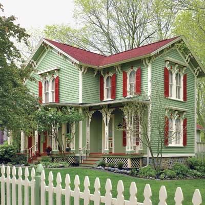 A green house with red shutters and garden outside of the house 