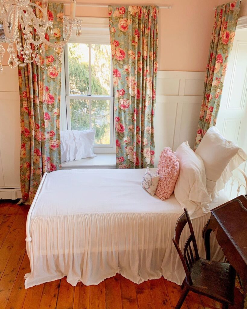 A pink bedroom with floral curtains and wooden floor and white bed
