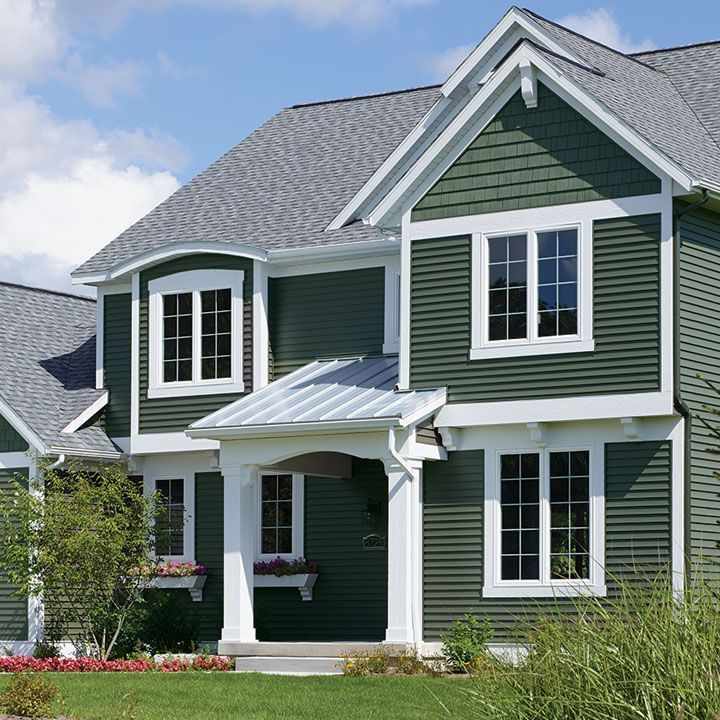 A green house with white windows and pillars and garden outside of the house 