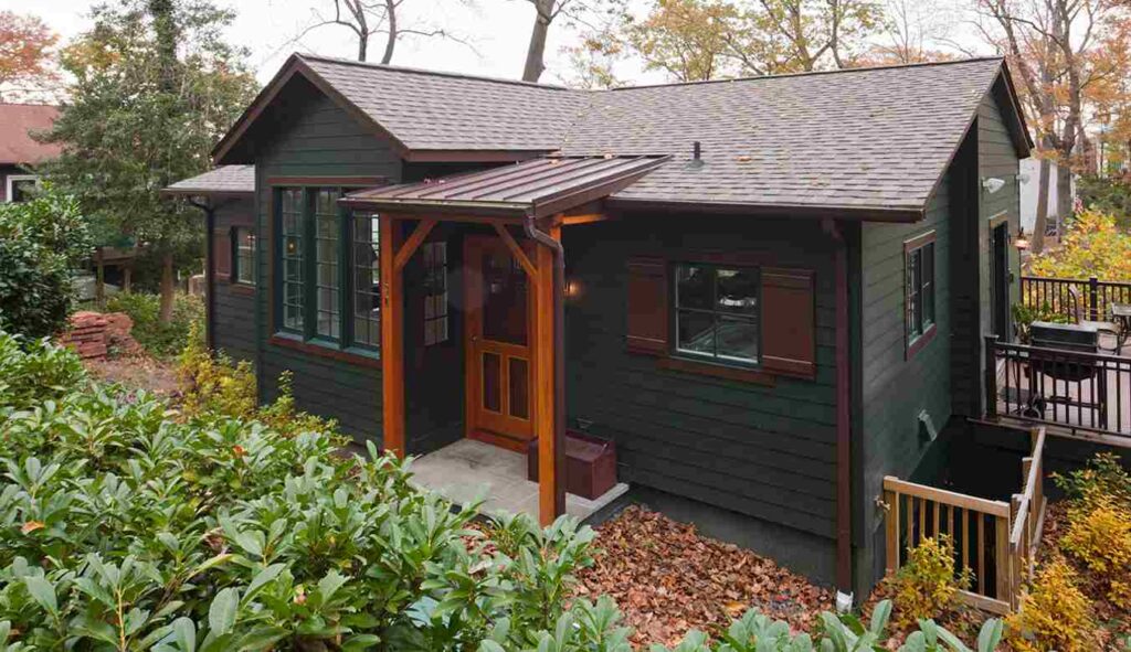 A green house with black trim and wooden pillars 