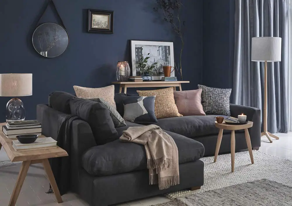 A blue living room with grey sofa and wooden table and mirror on the floor