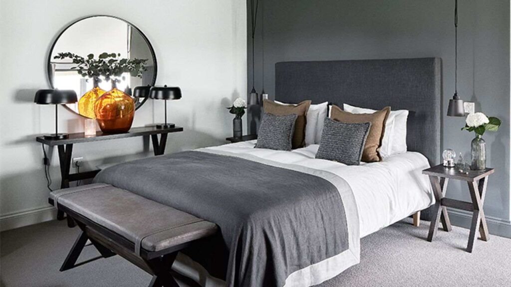 Grey bed frame and bedding and grey colored wall with a round black frame mirror