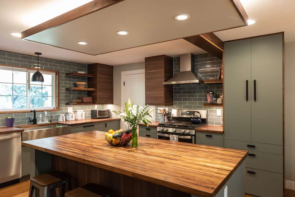 A sage green kitchen with wooden block and celling lights above the wall and glass windows