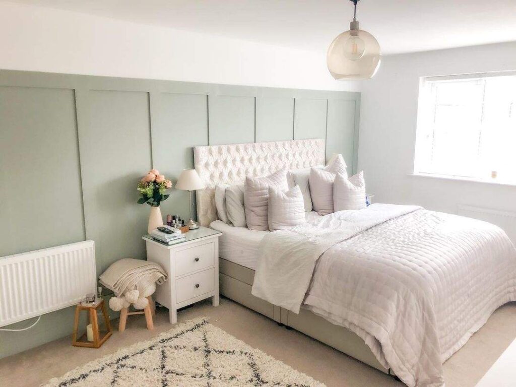 A sage green with white celling and bed with side table and wooden floor 
