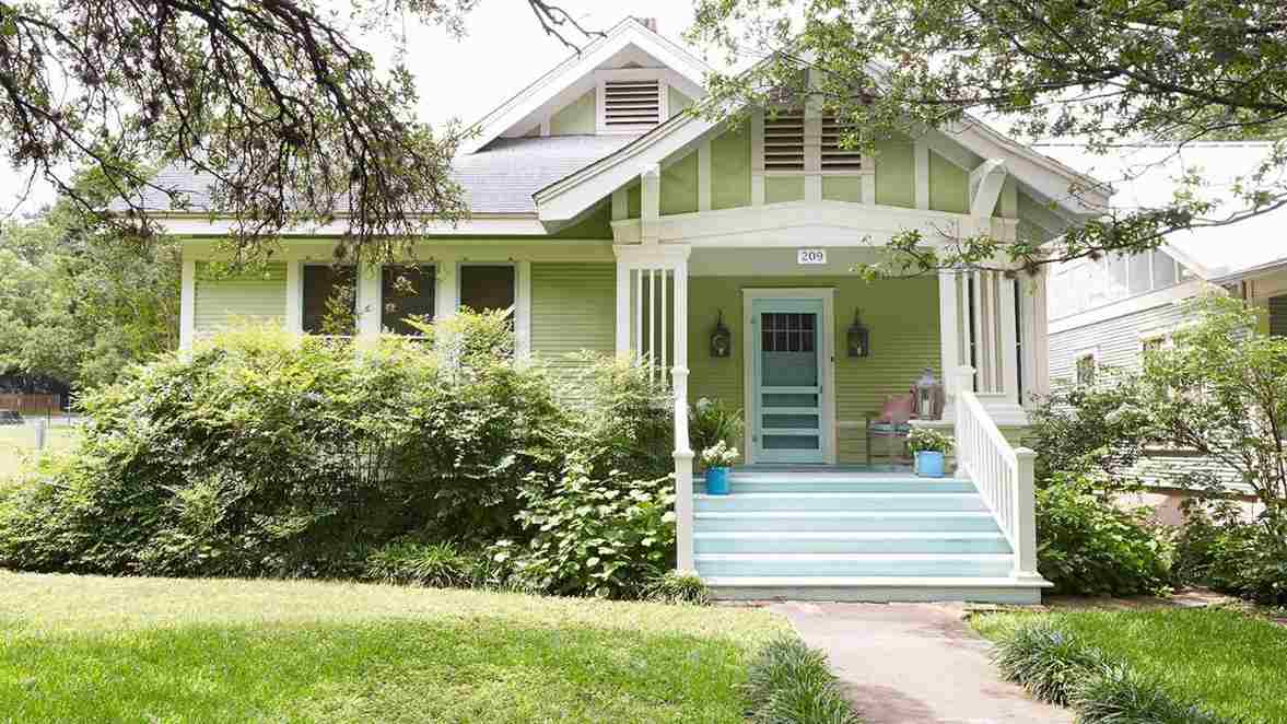 Light green home with shingles and plants around the house