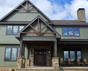 A green house with stone base pillars and black trim windows 