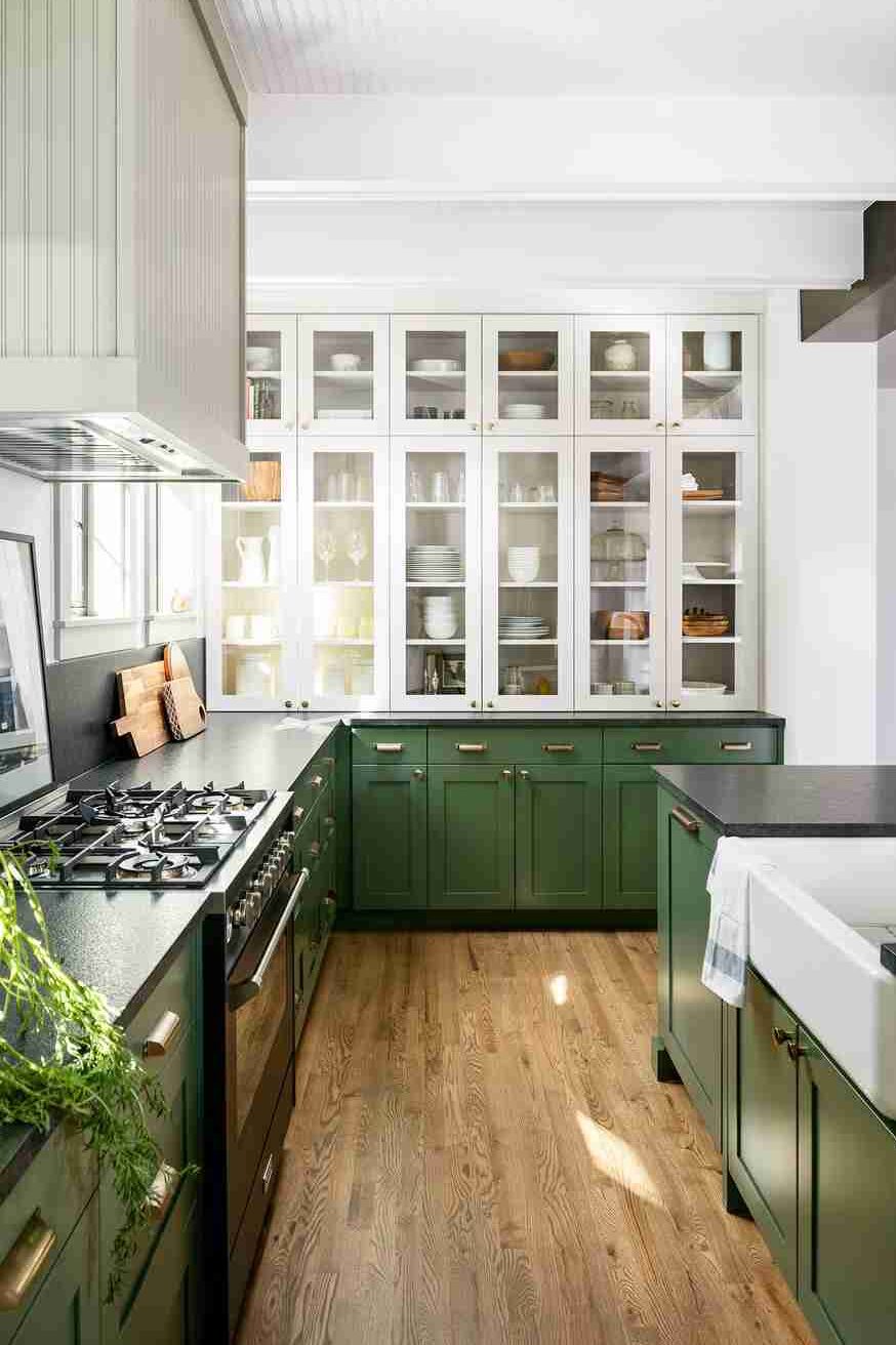 A sage green kitchen with white cabinets and black counter top