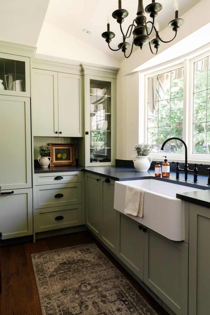 A sage green kitchen with black countertop and black fixtures