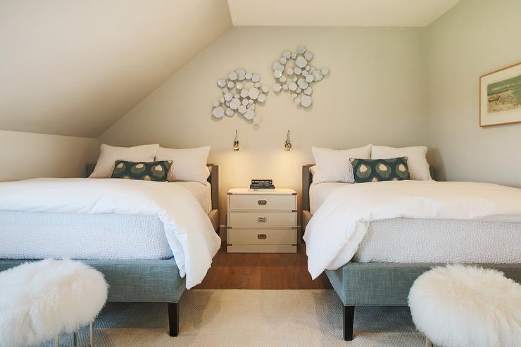 A bedroom with two beds and shared night stand and lights on the wall 