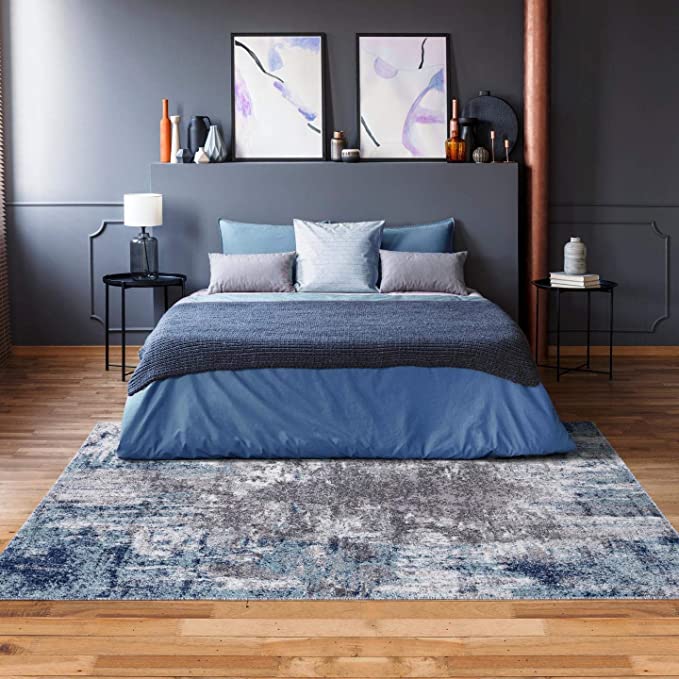 A bedroom with bed and grey blanket and pillow and wooden floor and rug on it