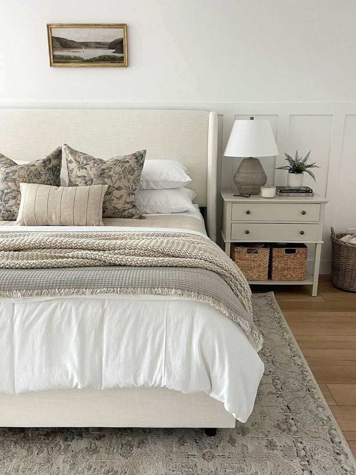 A bedroom with white bedding and pillows and throw and wooden floor and rug on it