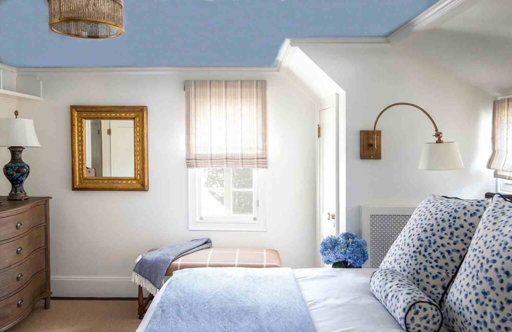 A white bedroom with blue celling and gold frame mirror on the wall