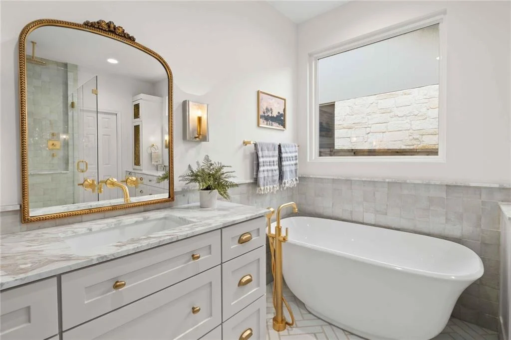 A bathroom with white cabinets with white counter top white gold fixtures 