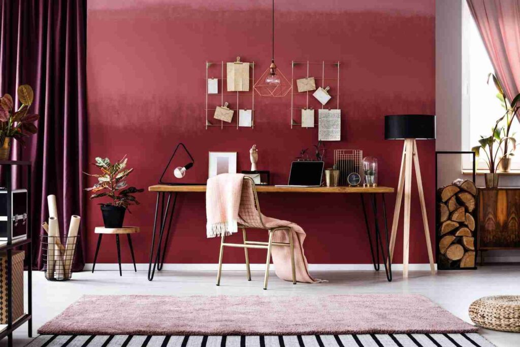 Burgundy colored wall with golden grid hanging and a wooden desk 