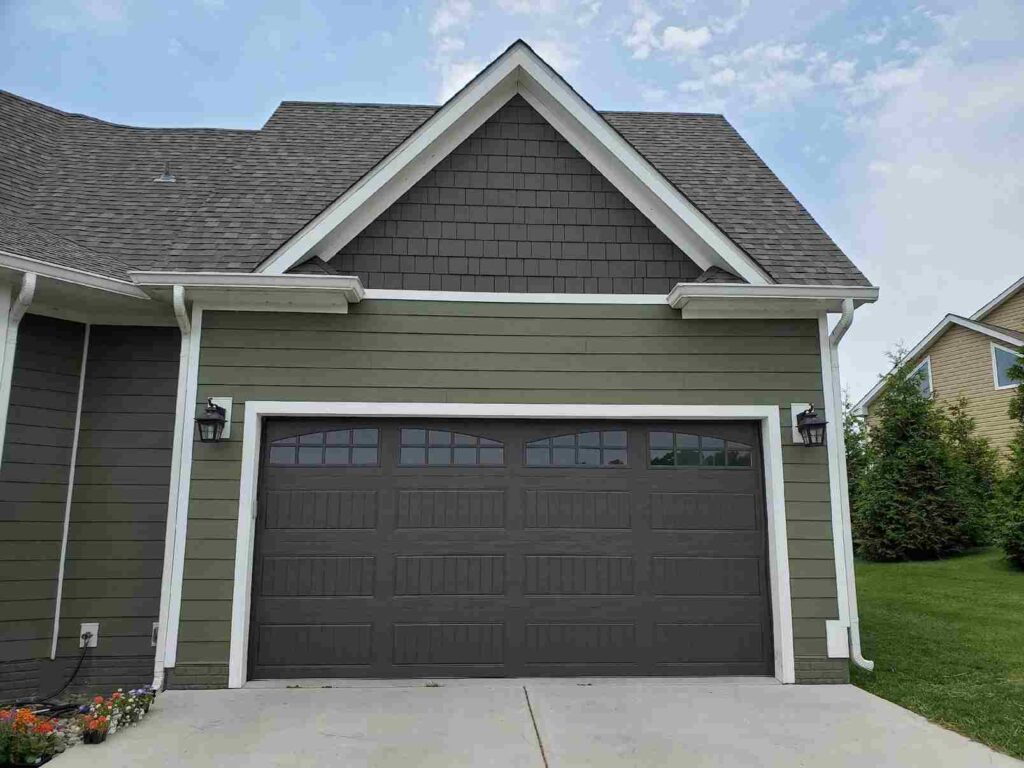 A green house with black garage door white trim 