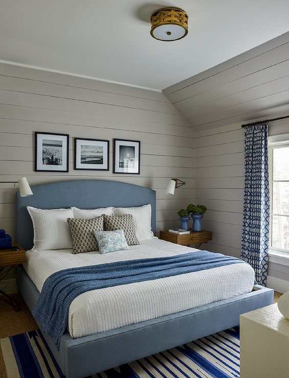 A grey bedroom with blue bed and black frames on the wall and windows with curtains