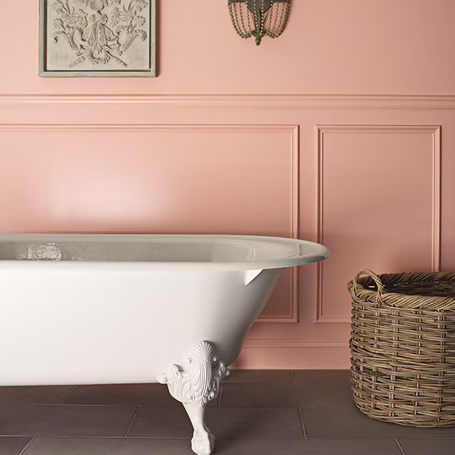 A pink wainscoting wall with white bathtub and woven baskets 