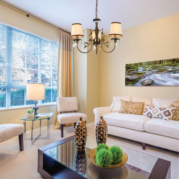 A beige living room with brass fixtures and sofa and tabla and lamp on the table 