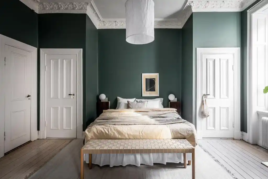 Dark green bedroom with white trim and wooden floor and white pillow and beige blankets on the bed