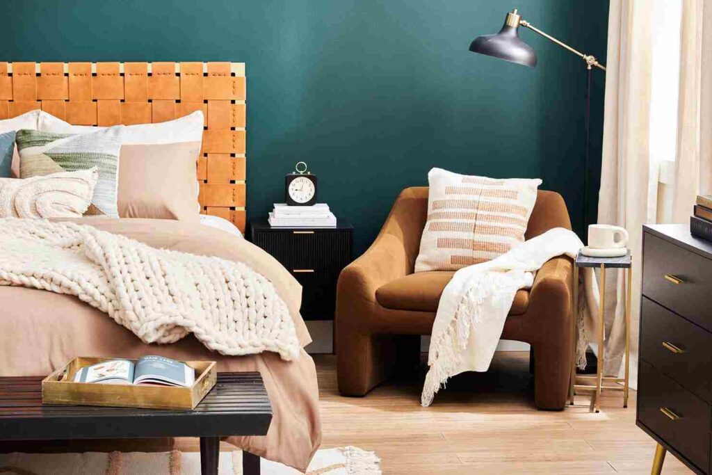 A bedroom with chair with pillow and throws and wooden floor 