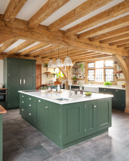 A dark sage green kitchen with grey flooring with wooden beams