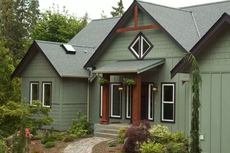 A sage green house with black trim and wooden pillars and windows 
