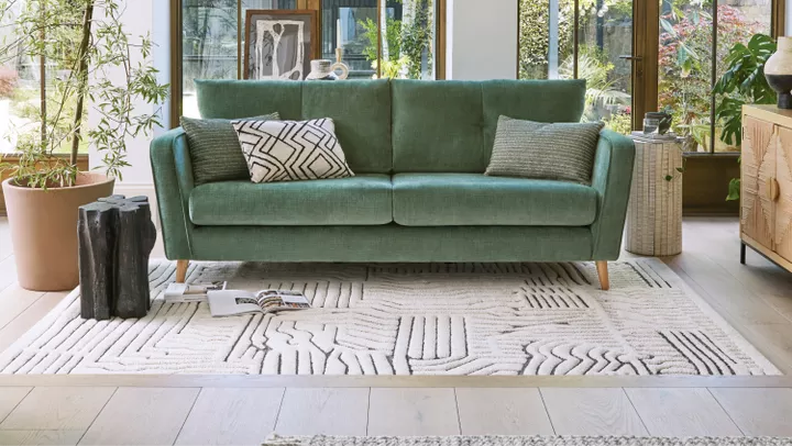 A sage green sofa with grey cushion and rug on the floor