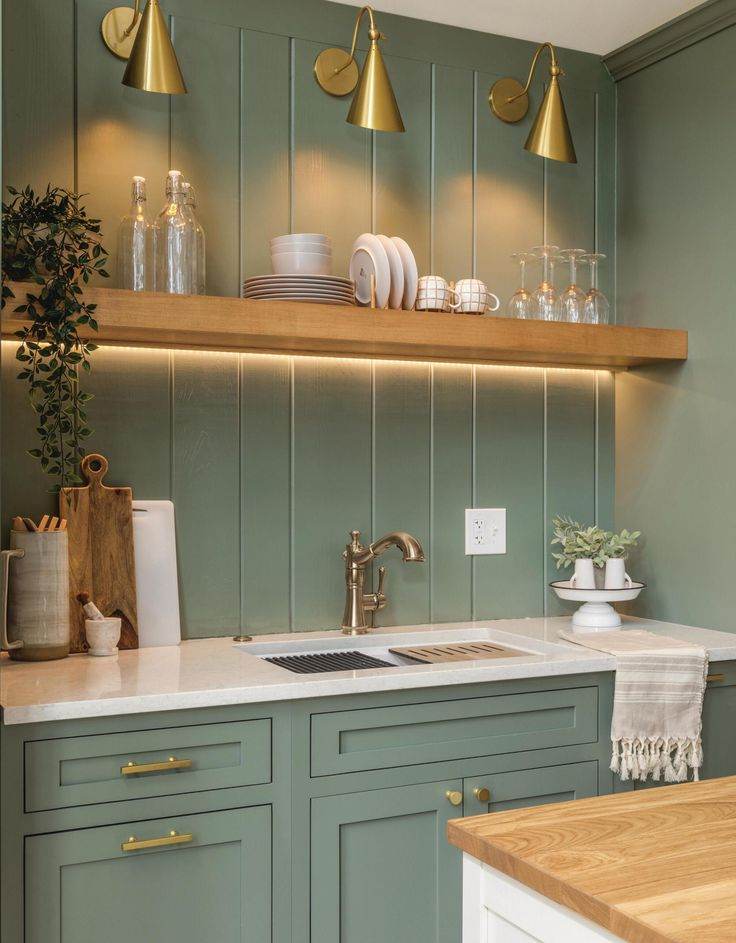 A sage green kitchen with under lights and brass fixtures