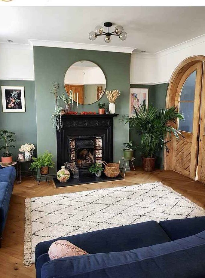 A sage green wall with mirror and wooden floor with rug