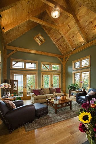A sage green living with wooden celling and wooden framed windows and sofa and table