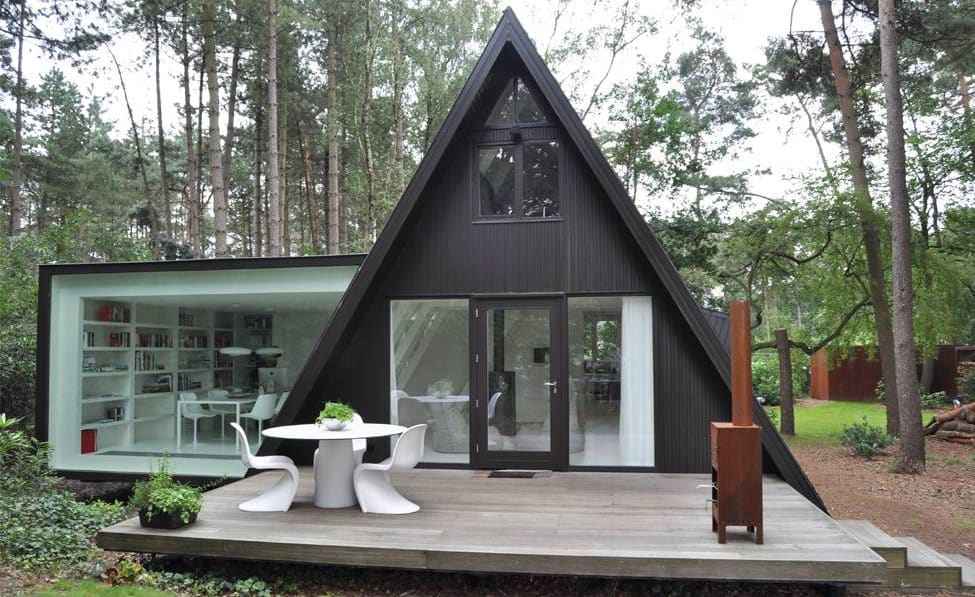 A grey cabin shaped house with glass windows and table outside of the house 