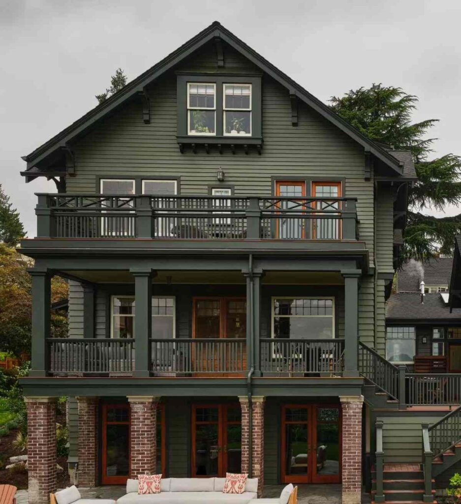 A green house with black balcony and wooden frame windows 