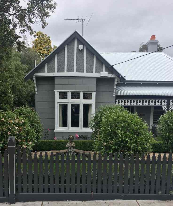 A grey house with white trim and  black fencing around the house 