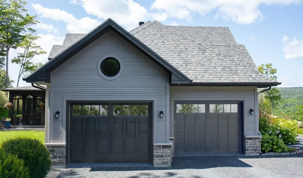 A grey house with black garage door and lights on the wall 