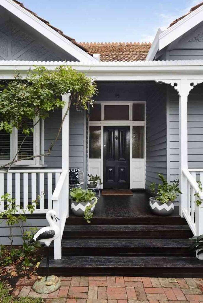A grey house with black porch and white door and plants outside of the house 