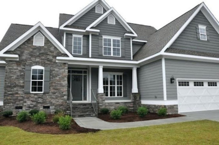 A light grey house with white trim and stone wall and garden outside of the house 