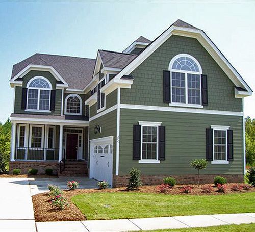 A green house with trim and black shutter and garden outside of the house 