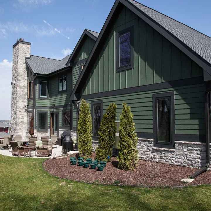 A green house with black trim and black frame windows and garden outside of the house