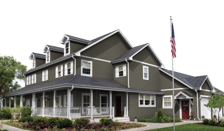 A olive green house with white trim and white pillars and garden outside of the house