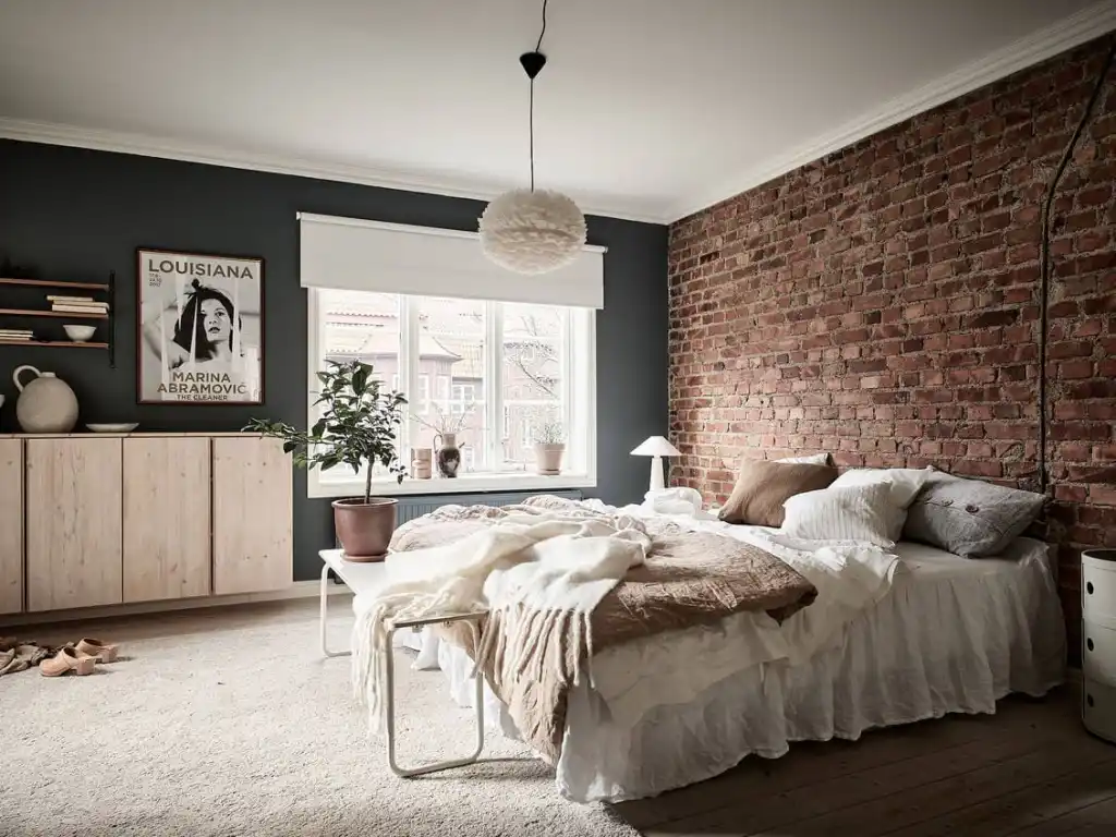 A navy bedroom with brick wall and and whit blankets and pillow