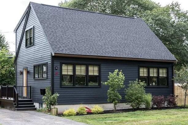 A blue house with black trim and windows and garden outside of the house 