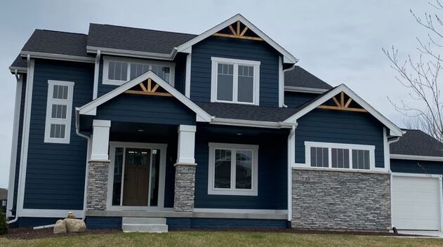 A blue house with stone cladding with white trim and window 