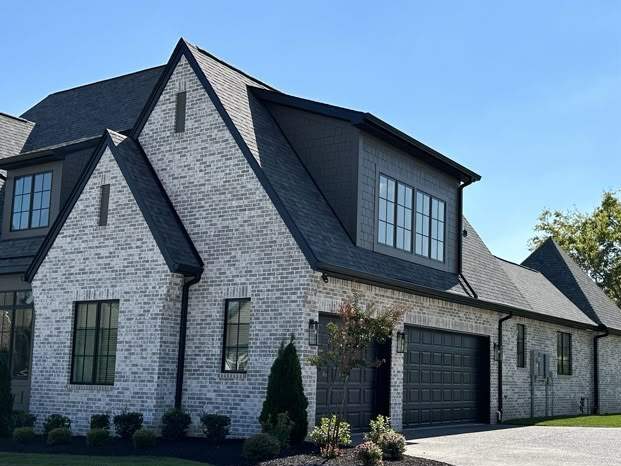 A grey brick house with black roof and windows and garage door 
