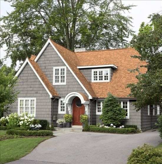 A grey house with brown roof and white trim and wooden door 