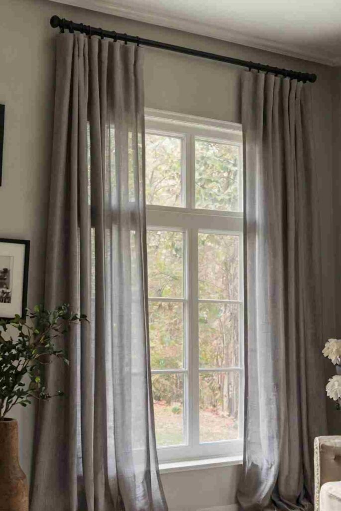 A grey living room with sheer curtains with windows 