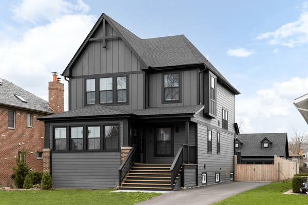 A grey house with black trim and glass windows and black railing and stair 